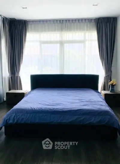 Spacious bedroom with large window and elegant curtains, featuring a cozy bed and stylish decor.