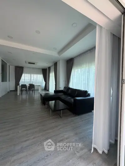 Spacious modern living room with sleek black sofa and large windows offering abundant natural light.