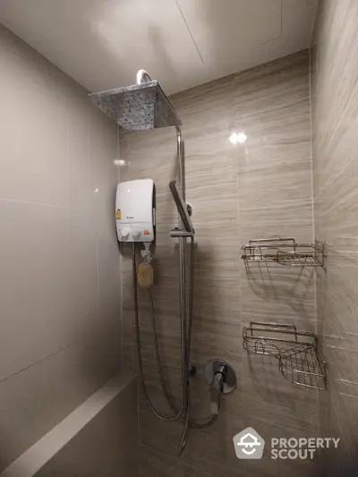 Modern bathroom with sleek beige tiles featuring a wall-mounted electric shower unit and convenient shelving, perfect for a refreshing and organized start to the day.