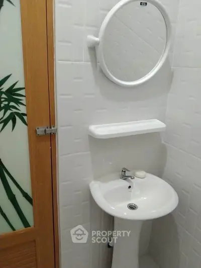 Compact bathroom with pedestal sink and round mirror, featuring modern white tile design.