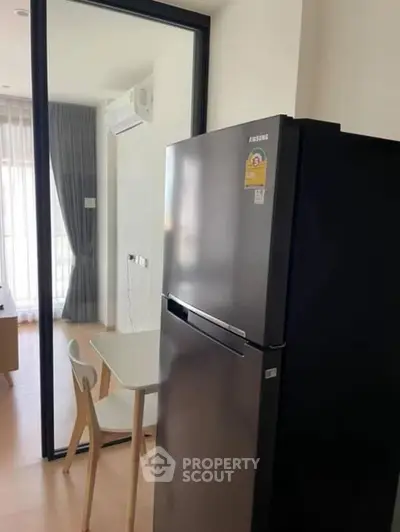 Modern apartment interior with sleek refrigerator and dining area near large window.