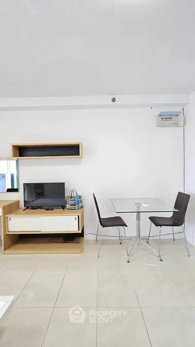 Modern living room with sleek furniture and minimalist design, featuring a TV and glass dining table.