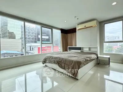 Spacious bedroom with city view and modern furnishings in high-rise apartment.