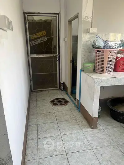 Compact kitchen area with tiled floor and basic amenities, featuring a door leading outside.