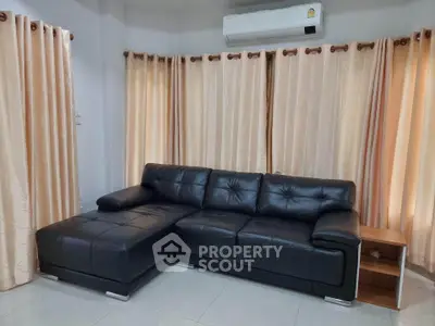 Spacious living room with elegant black leather sofa and large windows with beige curtains