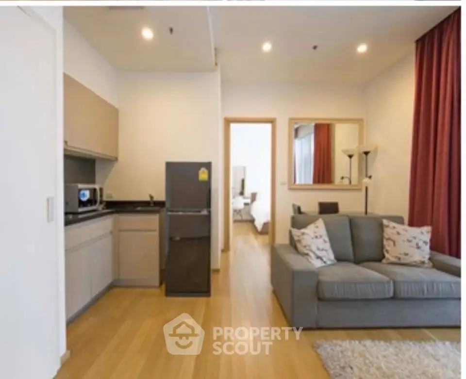 Modern living room with open kitchen, featuring sleek furniture and wooden flooring.