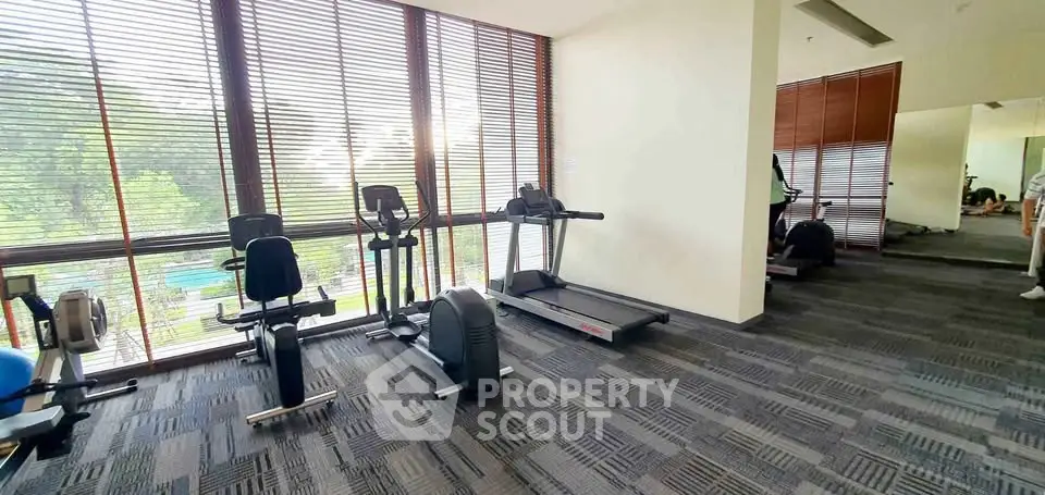 Spacious gym with modern equipment and large windows overlooking greenery.