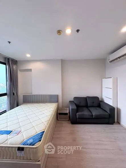 Modern bedroom with large window, cozy sofa, and air conditioning in a stylish apartment.