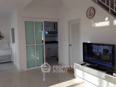 Modern living room with TV and sliding door to kitchen, featuring sleek white decor and tiled flooring.