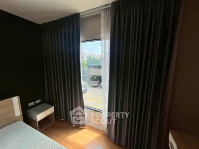 Cozy bedroom with large window and elegant curtains, offering a glimpse of the outside view.