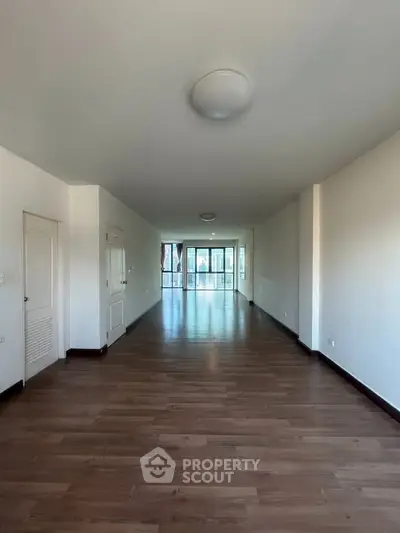 Spacious empty living room with wooden flooring and large windows for natural light.