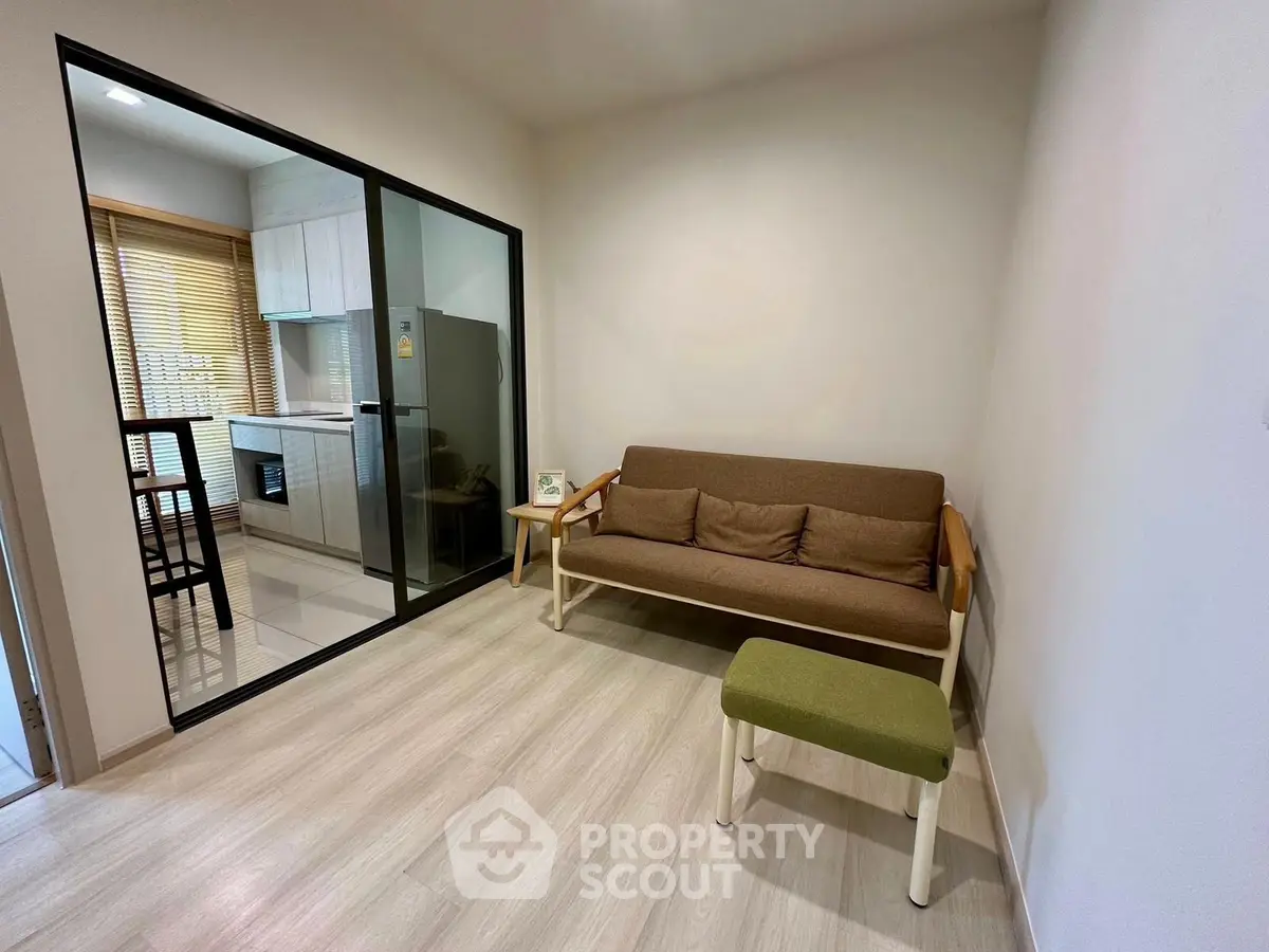Modern living room with cozy sofa and open kitchen layout, featuring sleek glass partition and stylish decor.