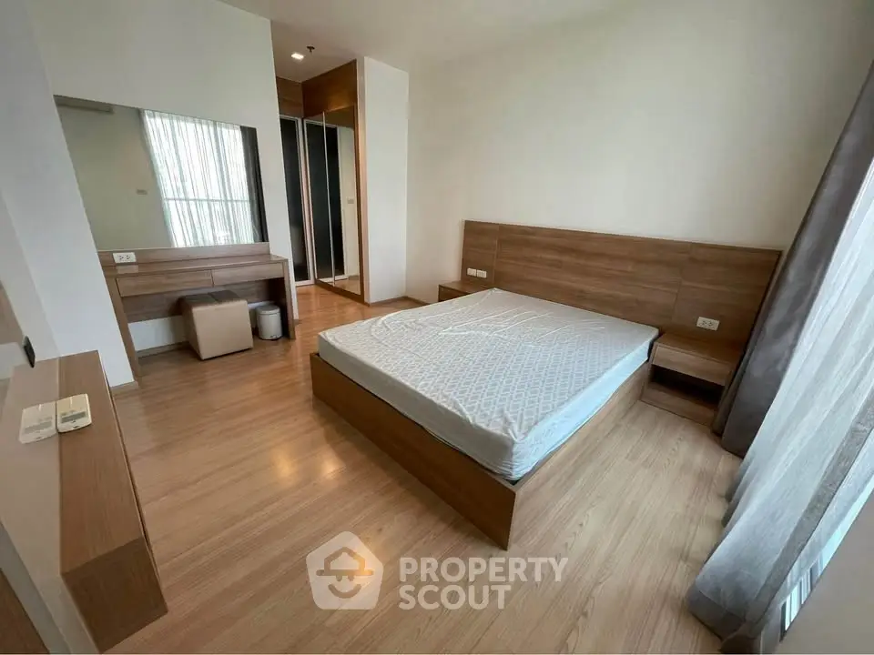 Spacious modern bedroom with wooden flooring and large window for natural light.
