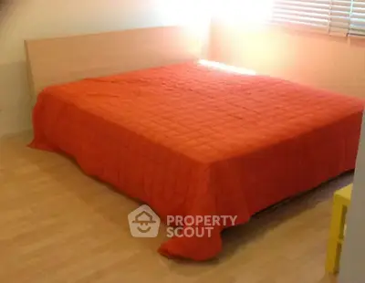 Cozy bedroom with vibrant orange bedspread and wooden flooring