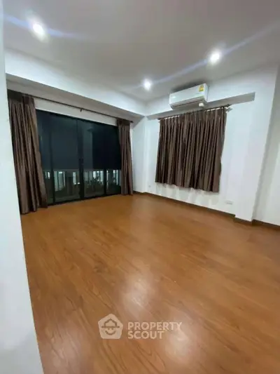 Spacious empty room with wooden flooring and large window, perfect for customization.
