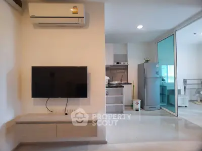 Modern apartment interior with wall-mounted TV and sleek kitchen featuring stainless steel fridge.