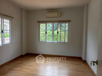 Spacious empty room with wooden flooring and large windows offering natural light.