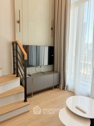 Modern living room with TV, stylish staircase, and large window for natural light.