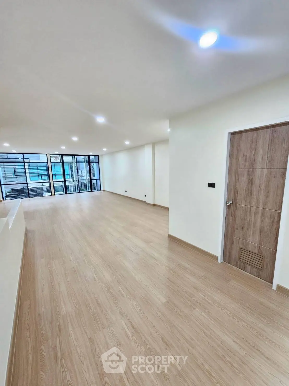 Spacious modern living room with wooden flooring and large windows for natural light.