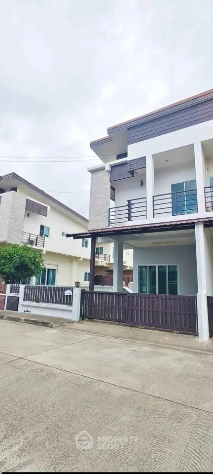 Modern two-story house with balcony and fenced yard in suburban neighborhood.