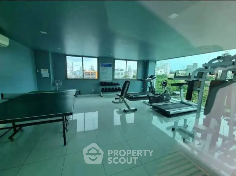 Spacious gym with modern equipment and city view in luxury apartment building.