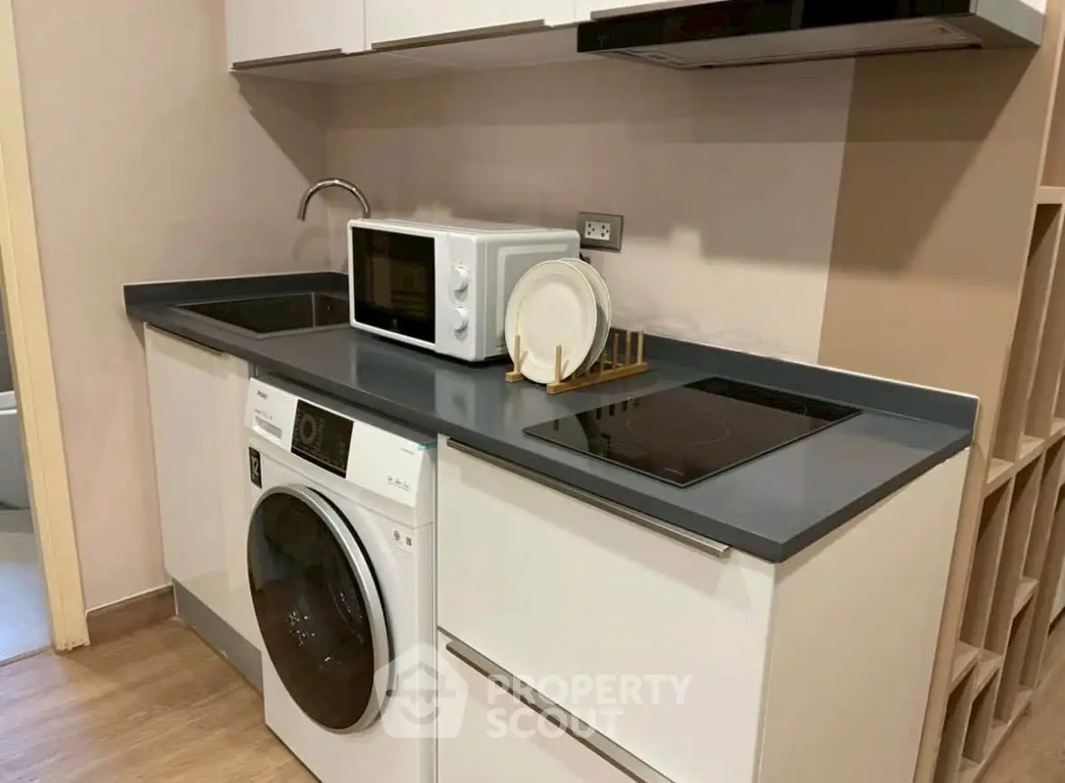 Modern kitchen with washing machine, microwave, and sleek countertops in compact layout.