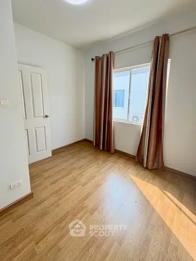 Bright empty room with wooden flooring and large window, perfect for customization.