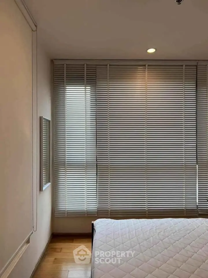 Cozy bedroom with wooden flooring and large window blinds.