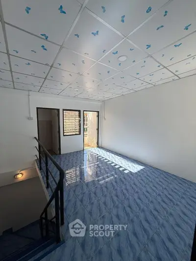 Spacious room with blue tiled floor and butterfly ceiling design, featuring natural light and stair access.