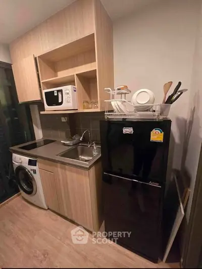 Modern compact kitchen with wooden cabinets, black fridge, and washing machine in a cozy apartment.