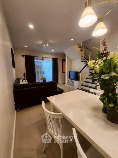 Modern living room with stylish decor and open dining area, featuring elegant lighting and cozy seating.