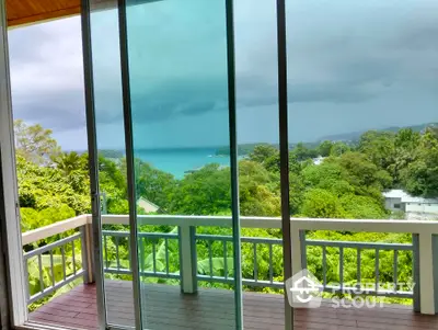 Stunning ocean view from a modern balcony with glass doors and lush greenery.