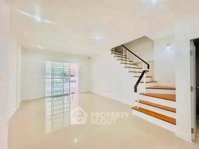 Spacious modern living room with sleek staircase and large windows for natural light.