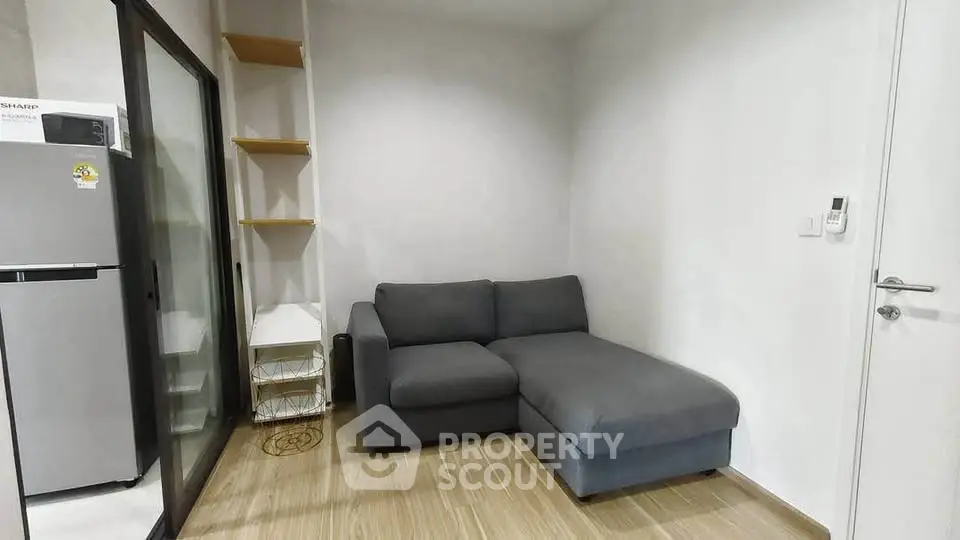 Modern living room with sleek gray sofa and wooden flooring, adjacent to a compact kitchen area.