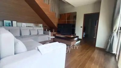 Modern living room with wooden flooring and stylish decor, featuring a large sectional sofa and a flat-screen TV.
