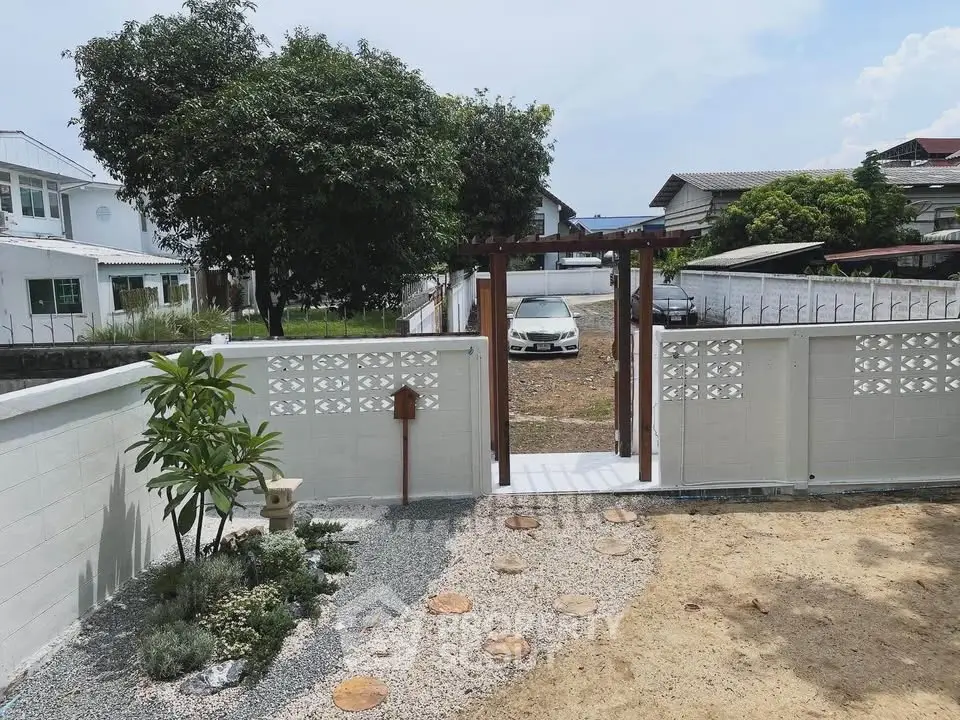Charming garden entrance with white fence and lush greenery in a serene neighborhood setting.
