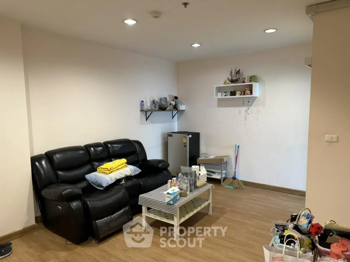 Cozy living room with black leather sofa and wooden flooring, perfect for relaxation.