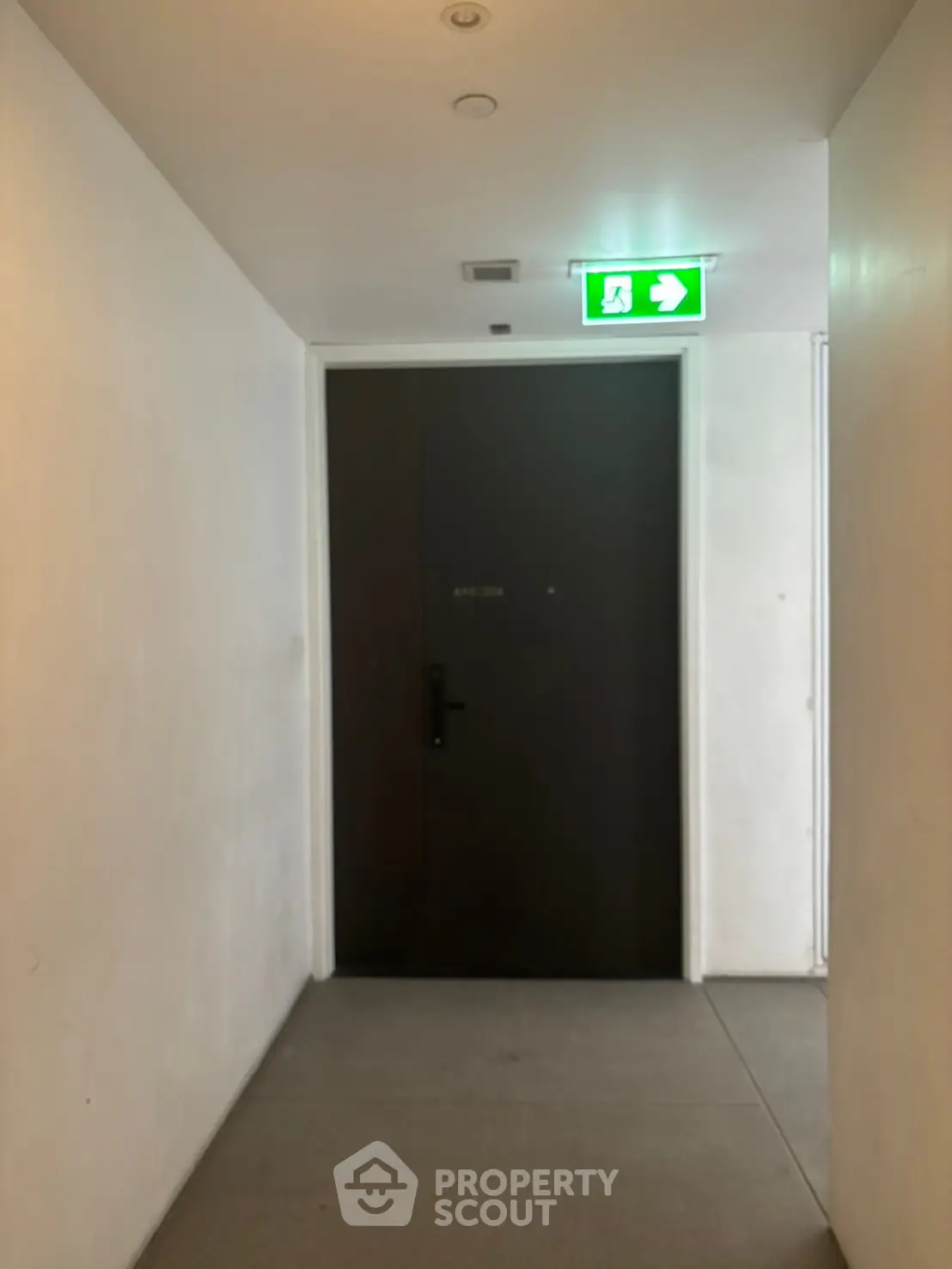 Modern apartment entrance with sleek dark door and emergency exit sign.