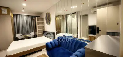 Modern studio apartment with stylish blue sofa and mirrored wall, featuring a cozy bed and dining area.