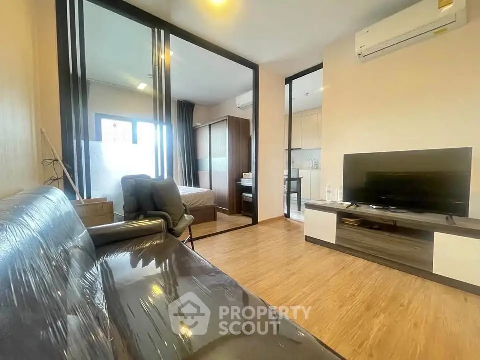 Modern living room with sleek furniture and open view into bedroom and kitchen