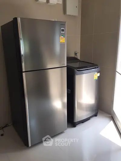 Modern kitchen with stainless steel fridge and washing machine in sleek interior.