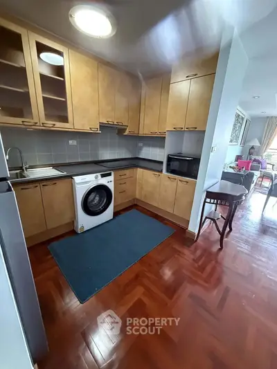 Charming kitchen with wooden cabinets and washing machine, open layout to living area, perfect for modern living.