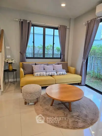 Charming living room with cozy yellow sofa, modern decor, and large windows offering garden views.
