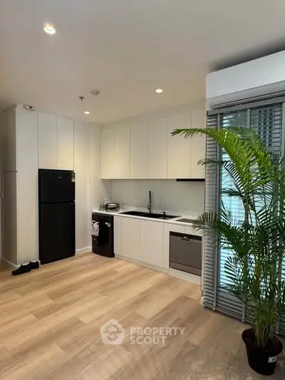 Modern kitchen with sleek white cabinets and wooden flooring, featuring a black fridge and lush indoor plant.
