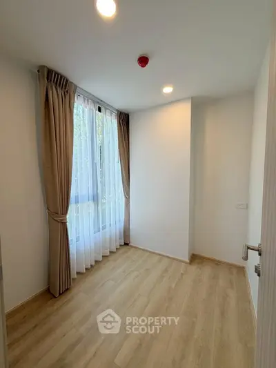Bright and airy empty room with large window and wooden flooring, perfect for customization.