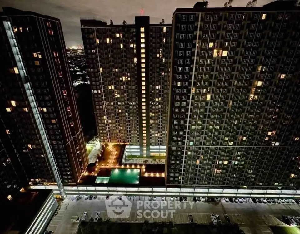 Stunning night view of modern high-rise apartment complex with illuminated windows and pool area.