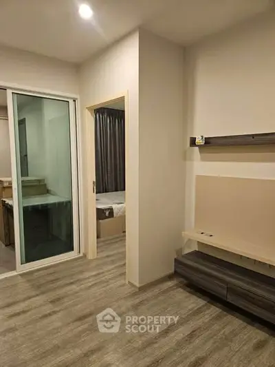 Modern apartment interior with wood flooring and sliding glass door leading to bedroom.