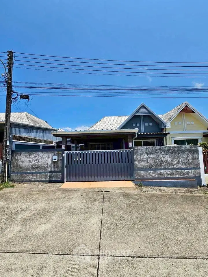 Charming single-story home with gated entrance and unique roof design under clear blue skies.