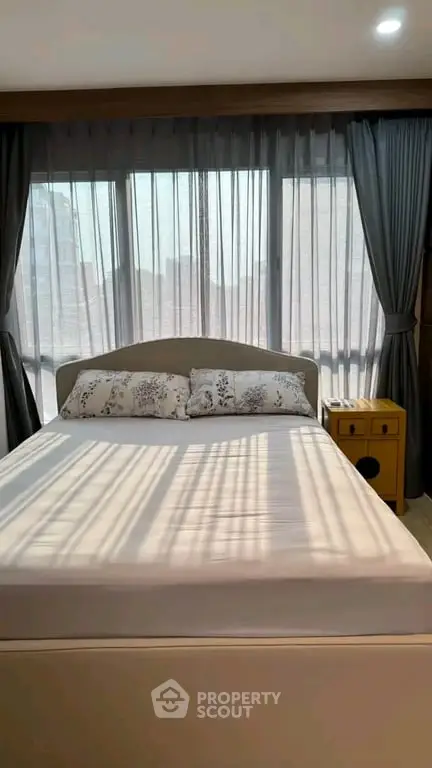 Spacious bedroom with large windows and elegant curtains, offering ample natural light and a cozy atmosphere.