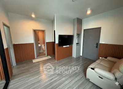 Modern living room with sleek flooring and wall paneling, featuring a mounted TV and cozy seating.